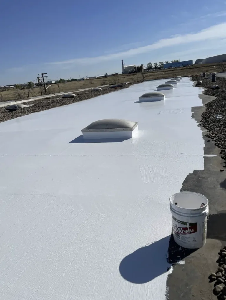 White roof coating applied around skylights on a long commercial roof