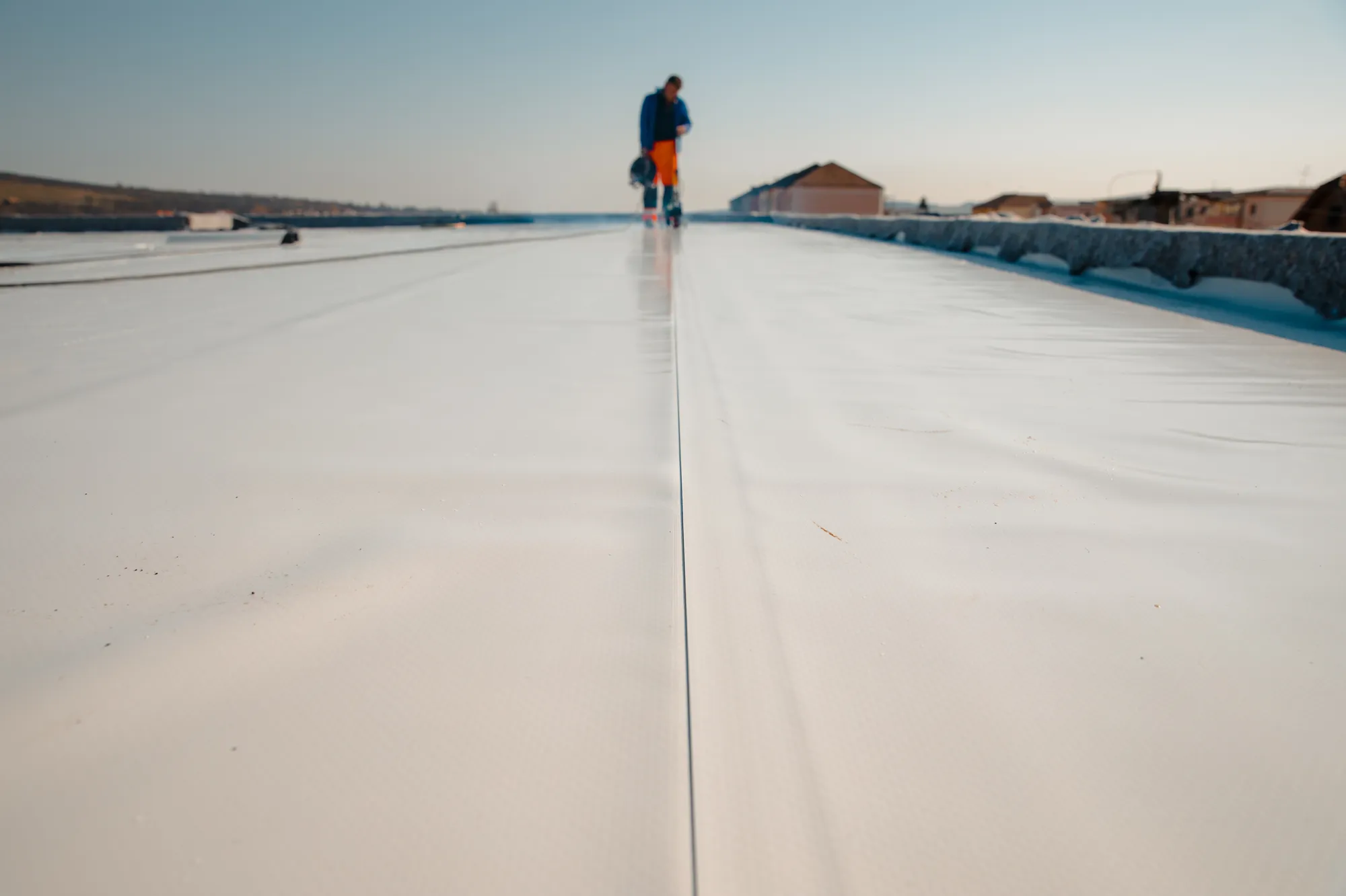 Crew member working on a long, freshly coated white commercial flat roof