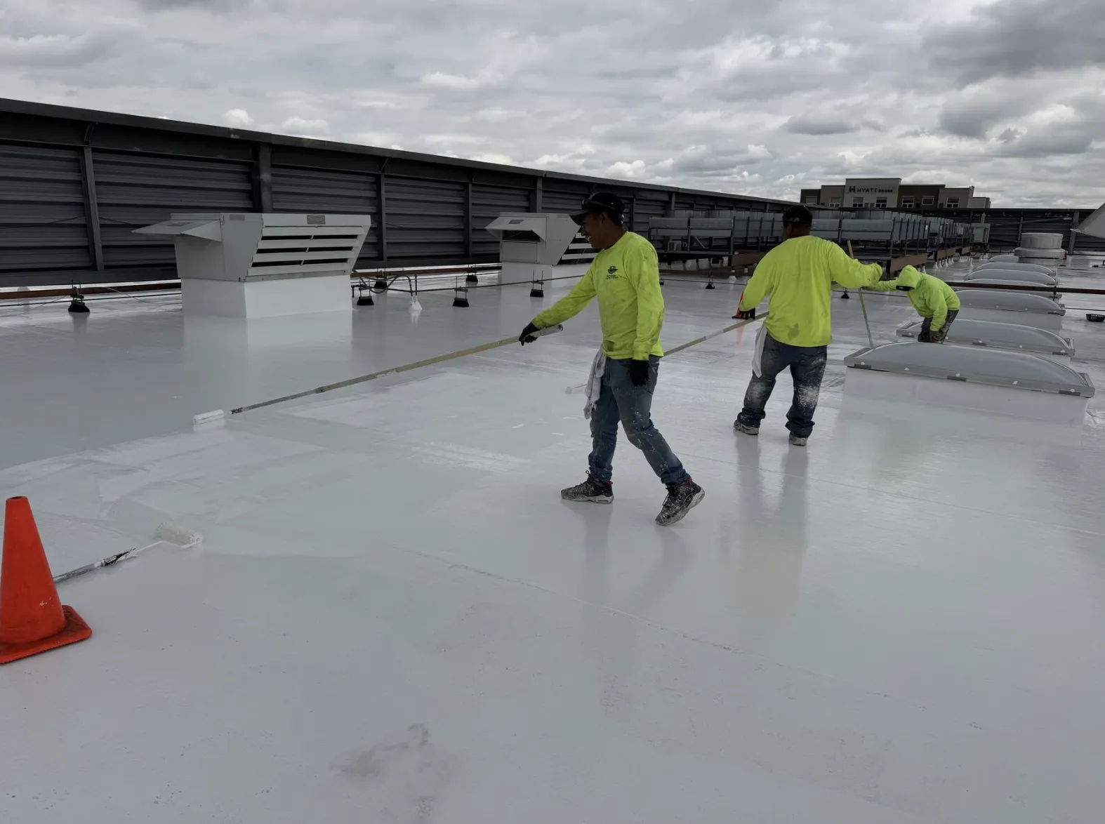 Two crew members in safety vests applying white coating to a commercial flat roof