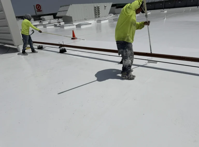 Roofer rolling white coating across a commercial flat roof