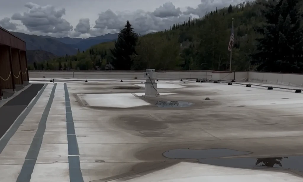 Aged commercial flat roof with ponding water and worn membrane before restoration