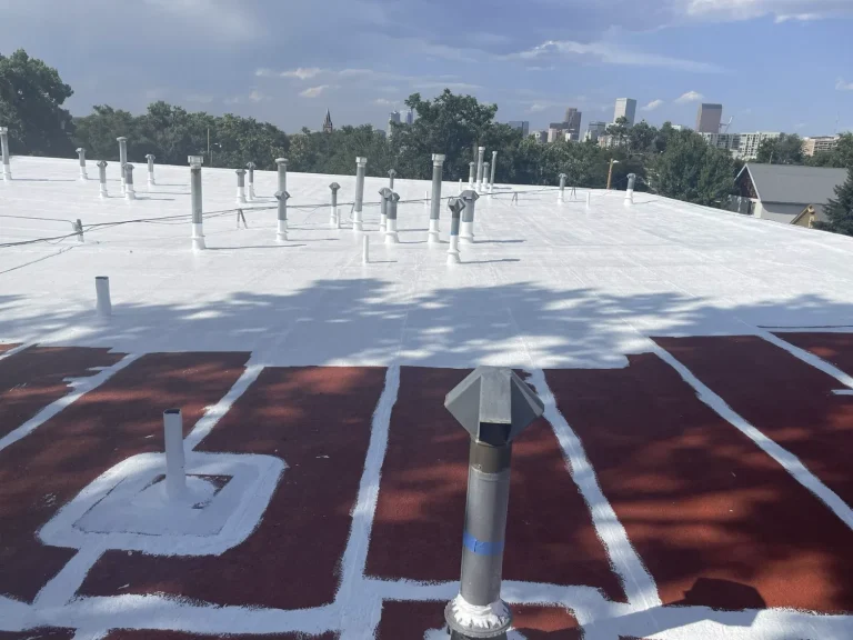 Flat roof with red primed field and white-coated seams around rooftop vents